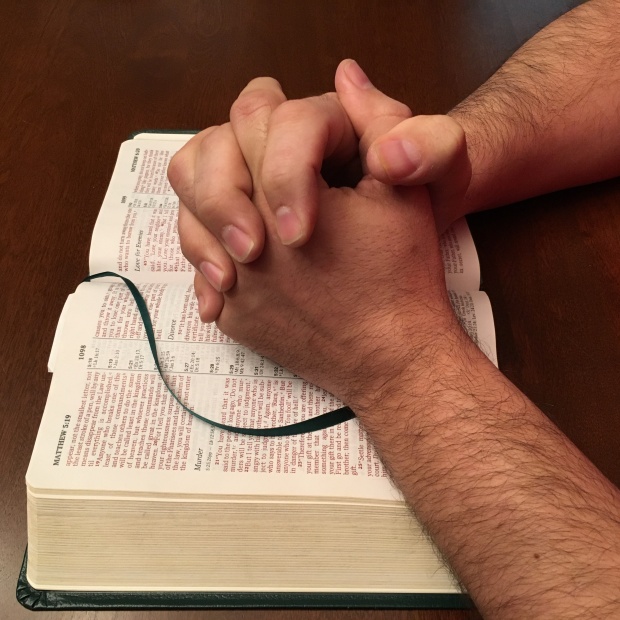 Hands resting on a Bible, folded in prayer